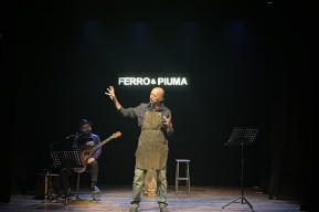 Foto del protagonista in piedi sul palco con un musicista alla chitarra alle sue spalle che lo accompagna